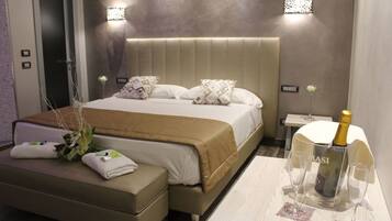 Une chambre d’hôtel moderne avec un grand lit, une table de chevet sur laquelle se trouve une bouteille de champagne, et une petite table avec deux verres.
