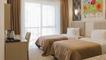A hotel room with two beds, a desk, and a large window with curtains.