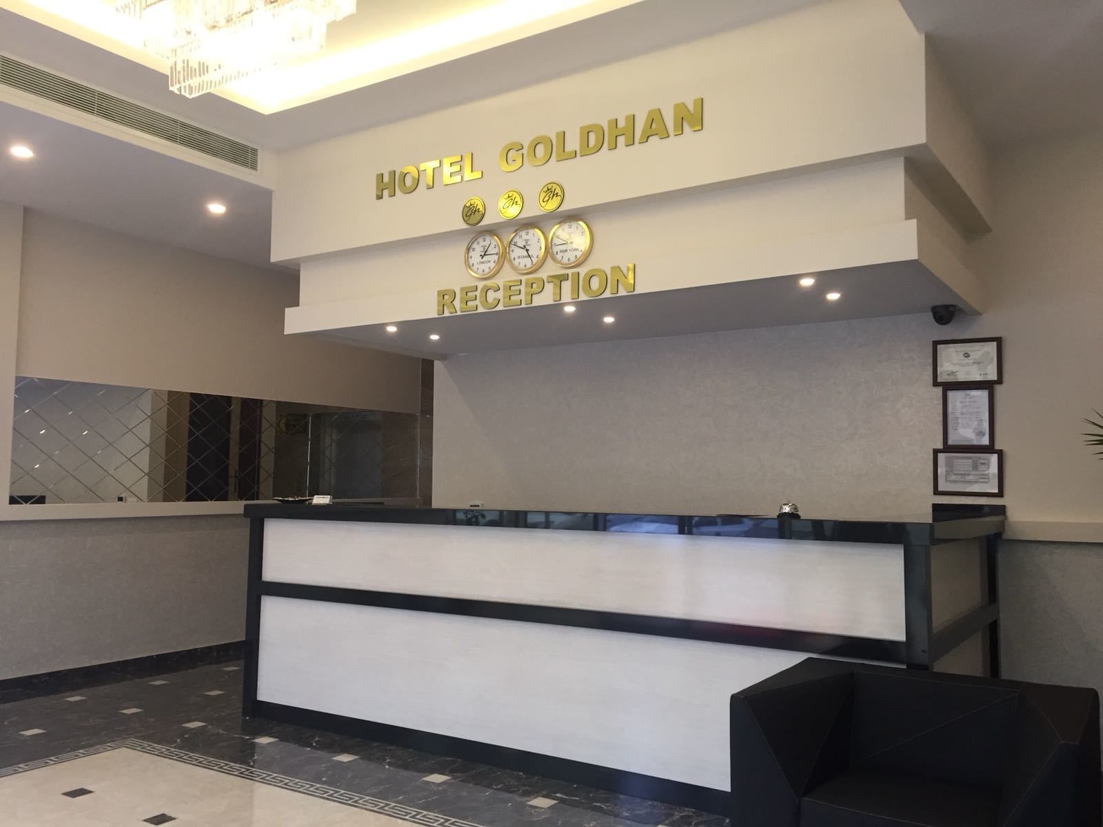 Zona de recepción de hotel con diseño moderno, que incluye un mostrador de recepción, una lámpara de araña y un reloj que muestra múltiples zonas horarias.