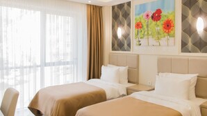 Una habitación de hotel con dos camas, un ventanal con cortinas y una obra de arte en la pared.