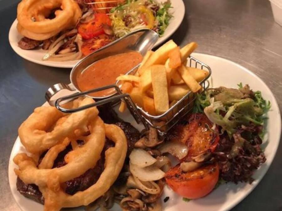 Een bord met een hamburger, uienringen, friet, een salade en een tomaat.