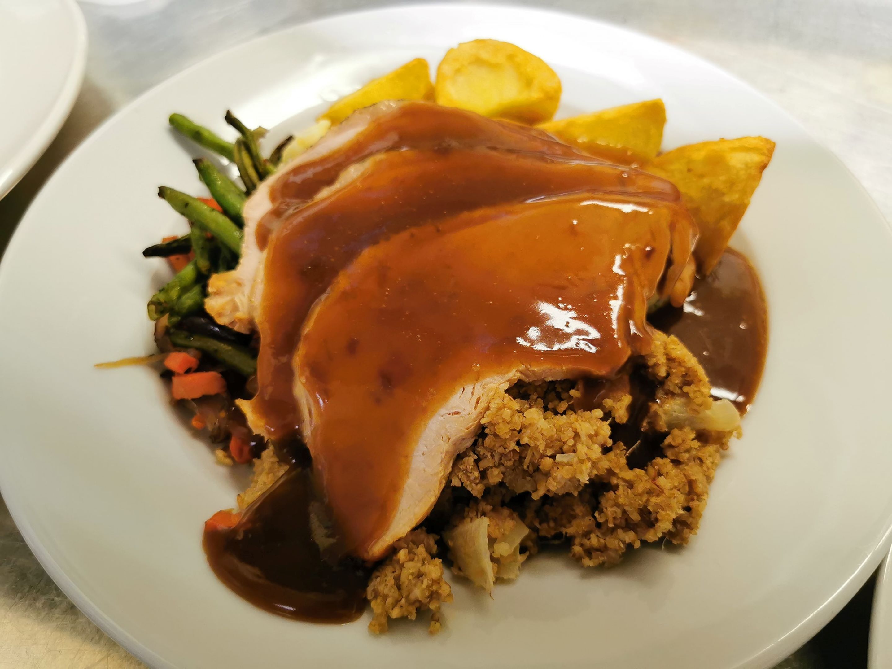 Un plato de comida con pechuga de pavo, salsa de gravy y verduras.