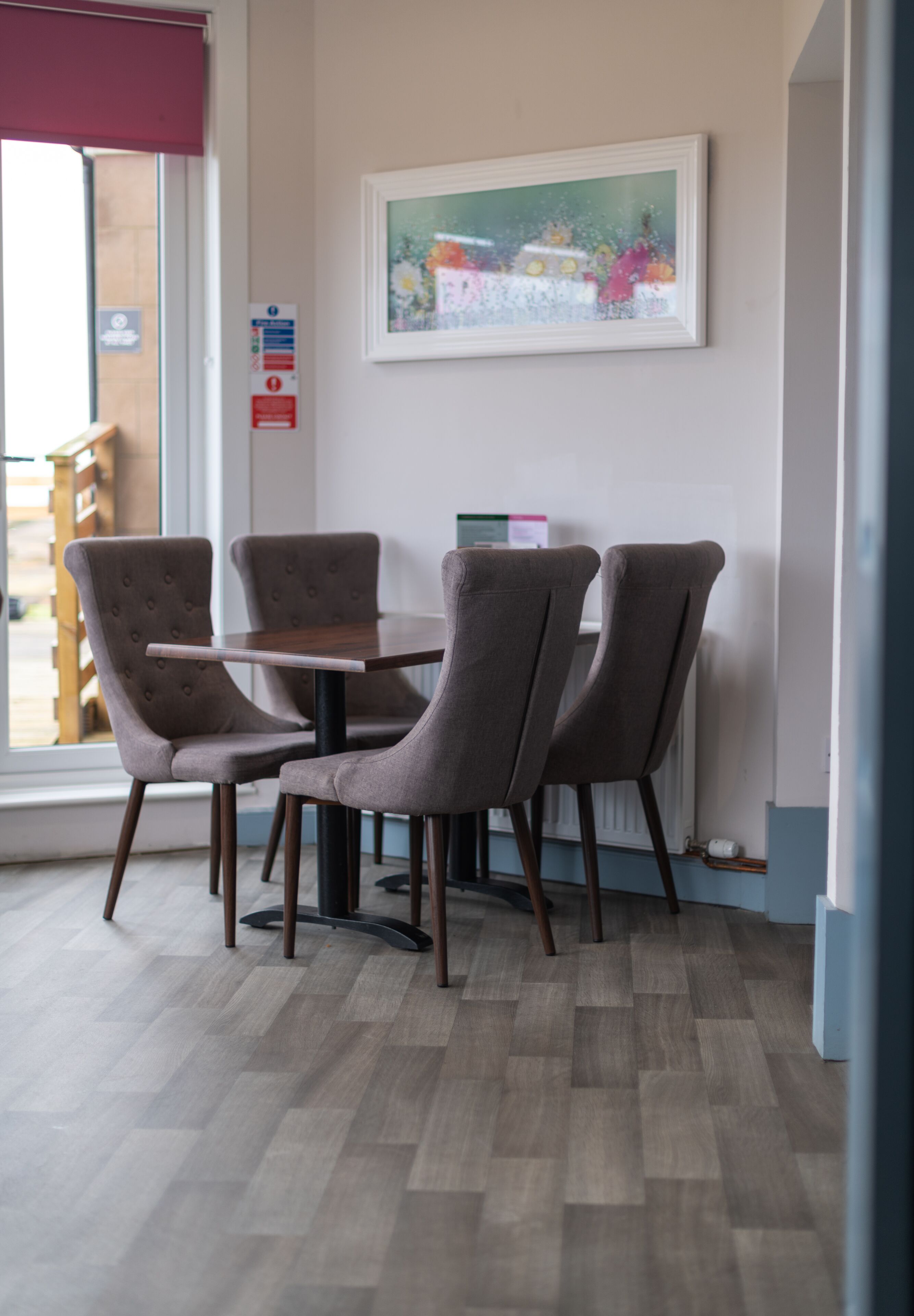 Un coin repas comprenant quatre chaises rembourrées et une table rectangulaire. Un tableau encadré est accroché au mur, au-dessus de la table.