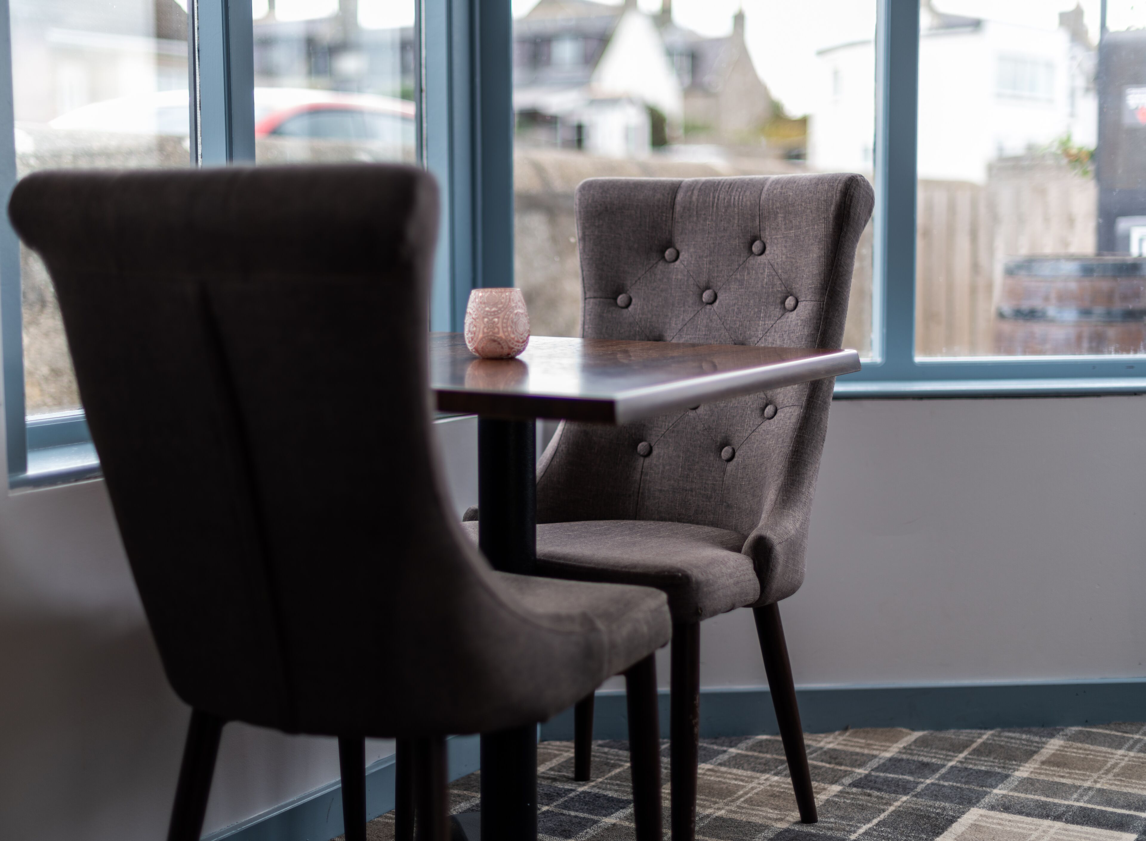 A modern dining area with a dark upholstered chair and a table, large windows offering a view of the outside.