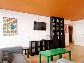 Un salon avec un canapé, une table verte, un téléviseur et une bibliothèque.