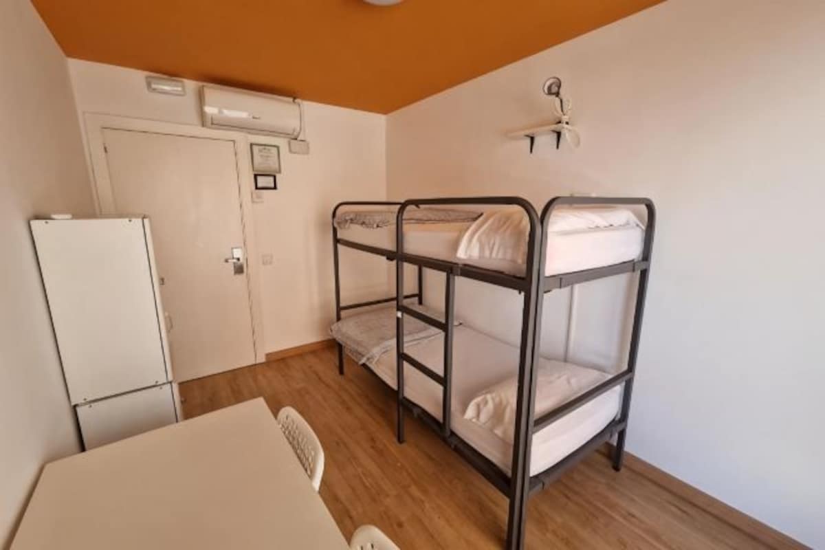 A bunk bed room with a white refrigerator, a table, and a chair.