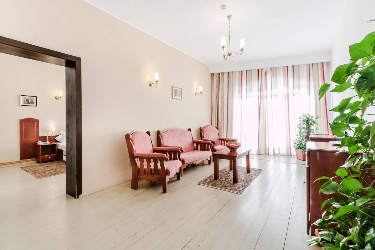 Ein geräumiges Wohnzimmer mit Holzboden, einer Sofagarnitur, einem Couchtisch und einem großen Fenster mit Vorhängen.
