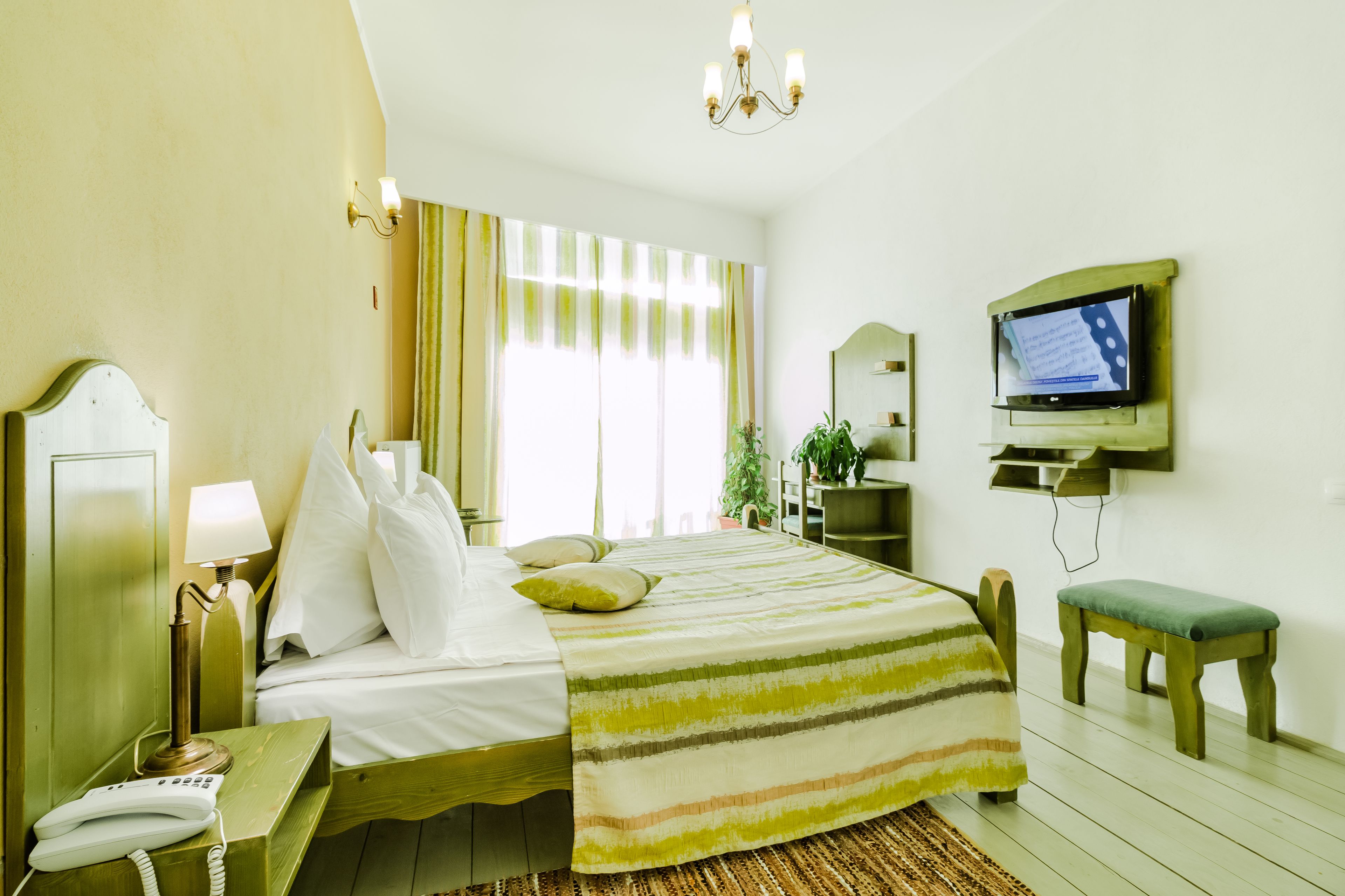 A hotel room with a bed, bedside lamp, telephone, television, and a small bench.