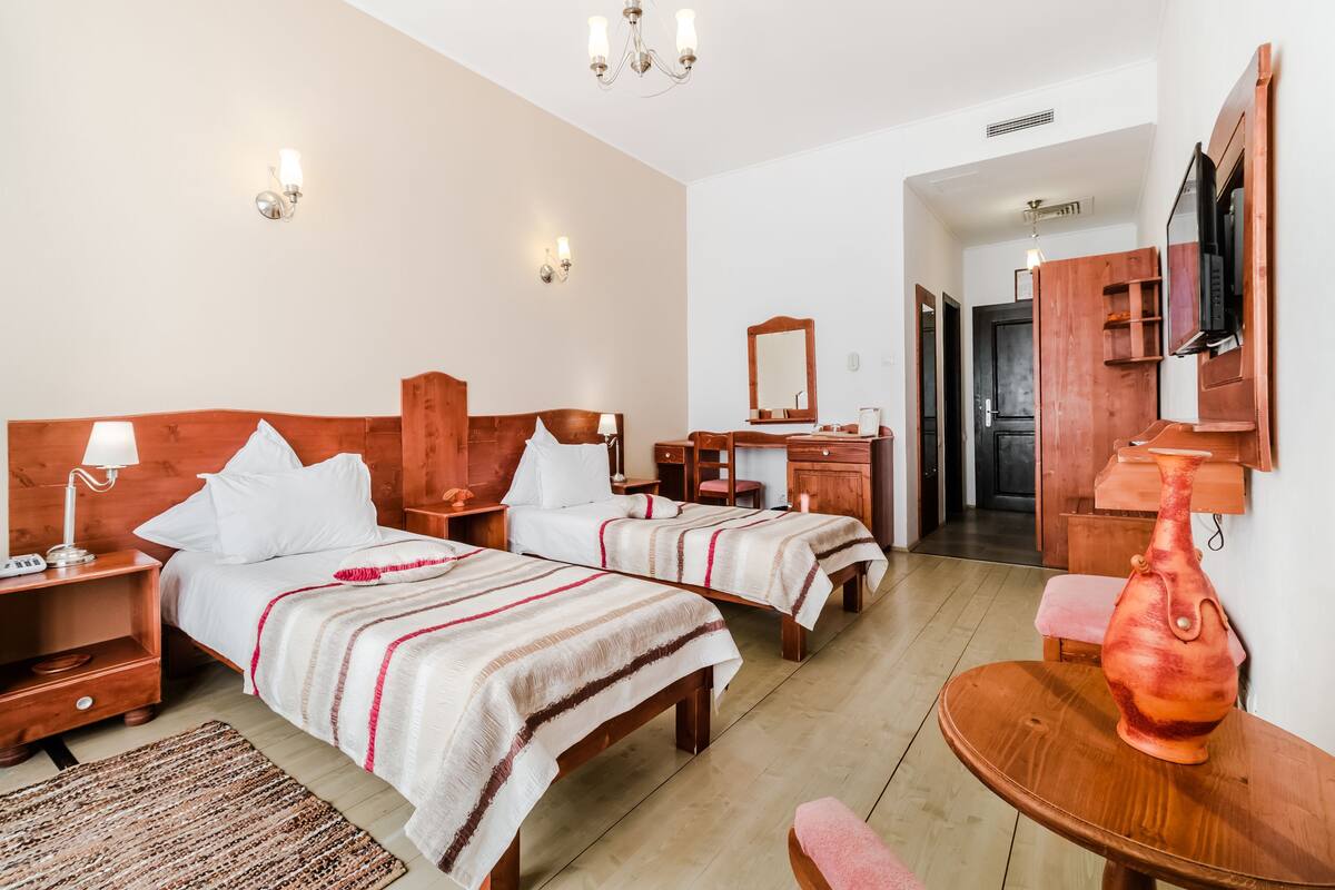 Ein Hotelzimmer mit zwei Betten, einem Holzkopfende, Nachttischen, einem Beistelltisch, einem Tisch mit einer Vase und einem Spiegel an der Wand.