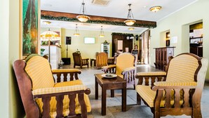 A lobby with wooden chairs and tables, a large painting on the wall, and a reception desk. - Ezio Brasov (Sacele)