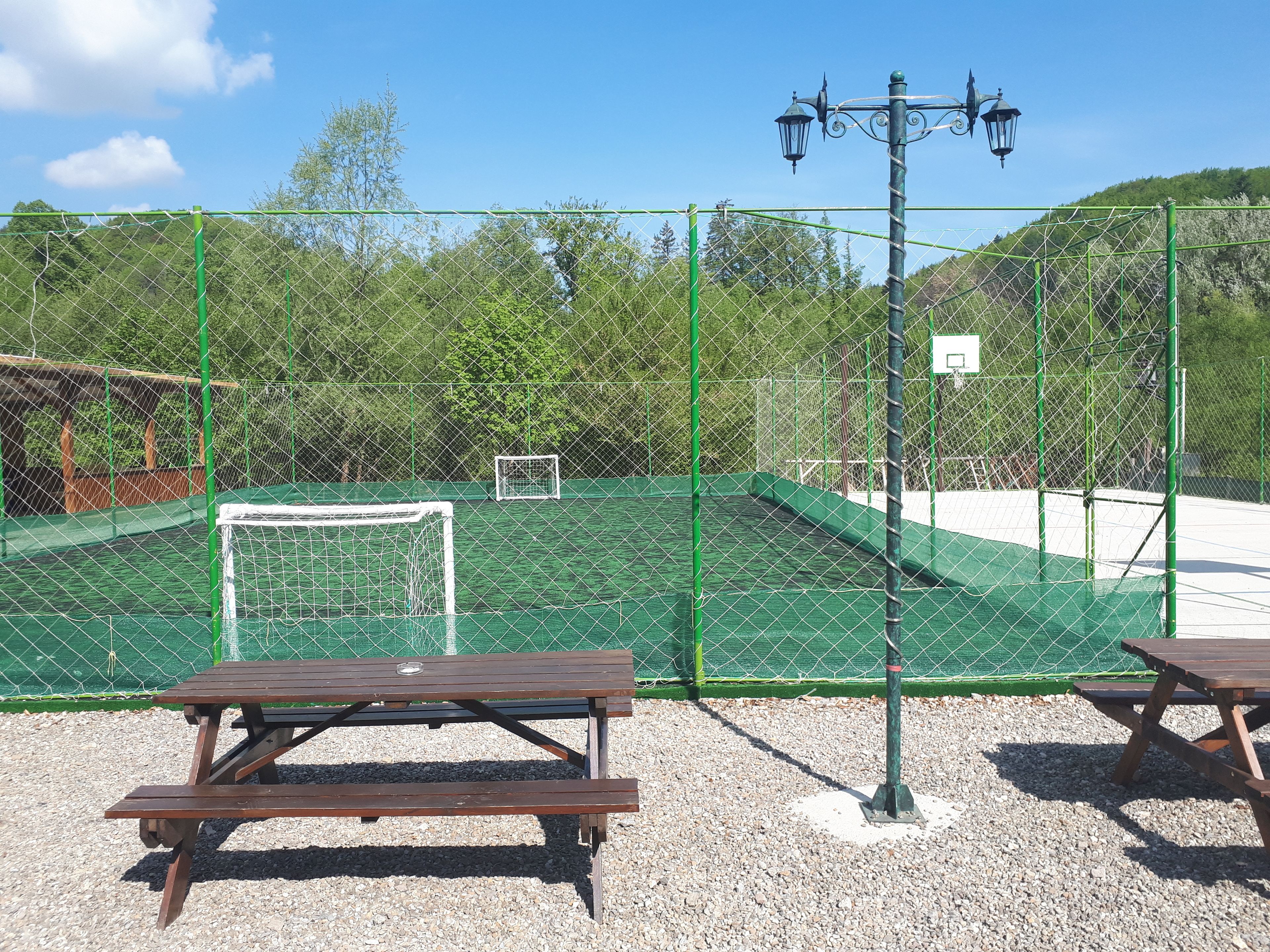 A fenced tennis court with a goal post, picnic tables, and a lamp post.