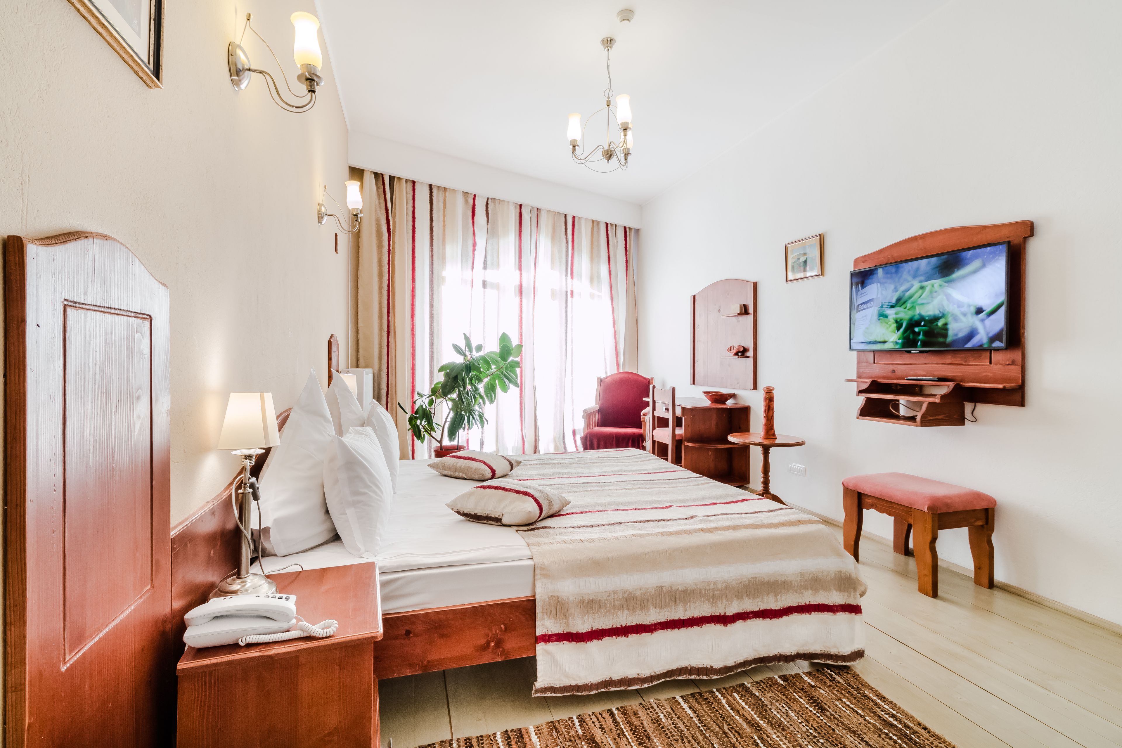 A hotel room with a bed, bedside table, lamp, TV, and a small table with a chair.