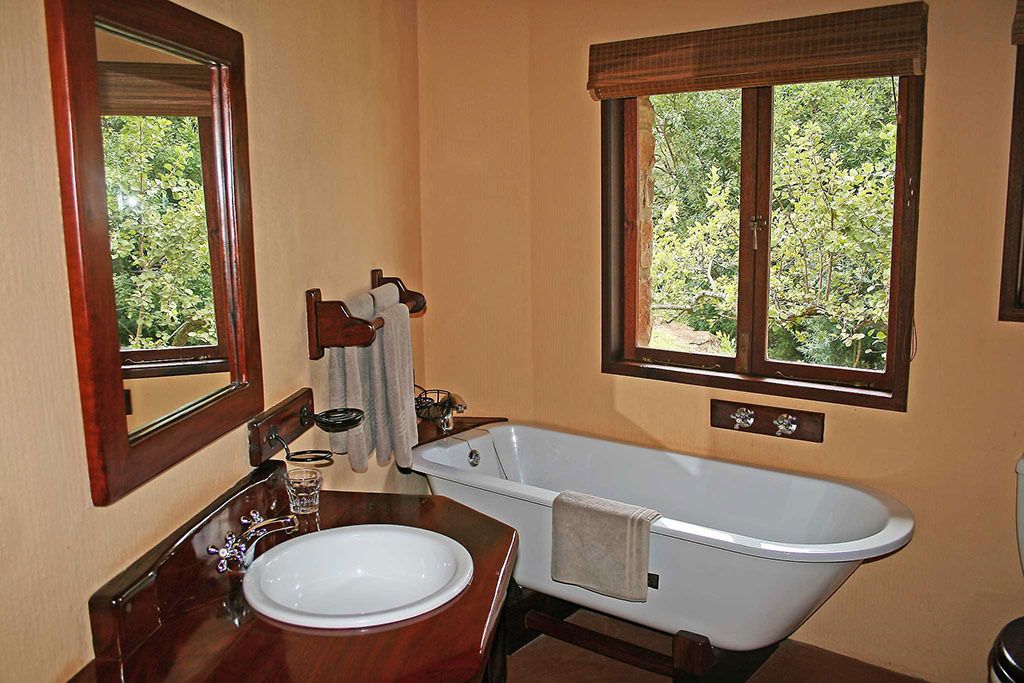 Ein Badezimmer mit freistehender Badewanne, einem Waschbecken mit Spiegel und einem Fenster mit Blick auf Grünflächen.