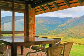 A dining area with a table and chairs, large windows, and a view of mountains. - Verlorenkloof Estate (Mashishing)