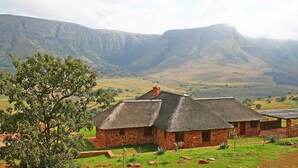 A stone house with a thatched roof, surrounded by a grassy landscape and a mountain in the background.