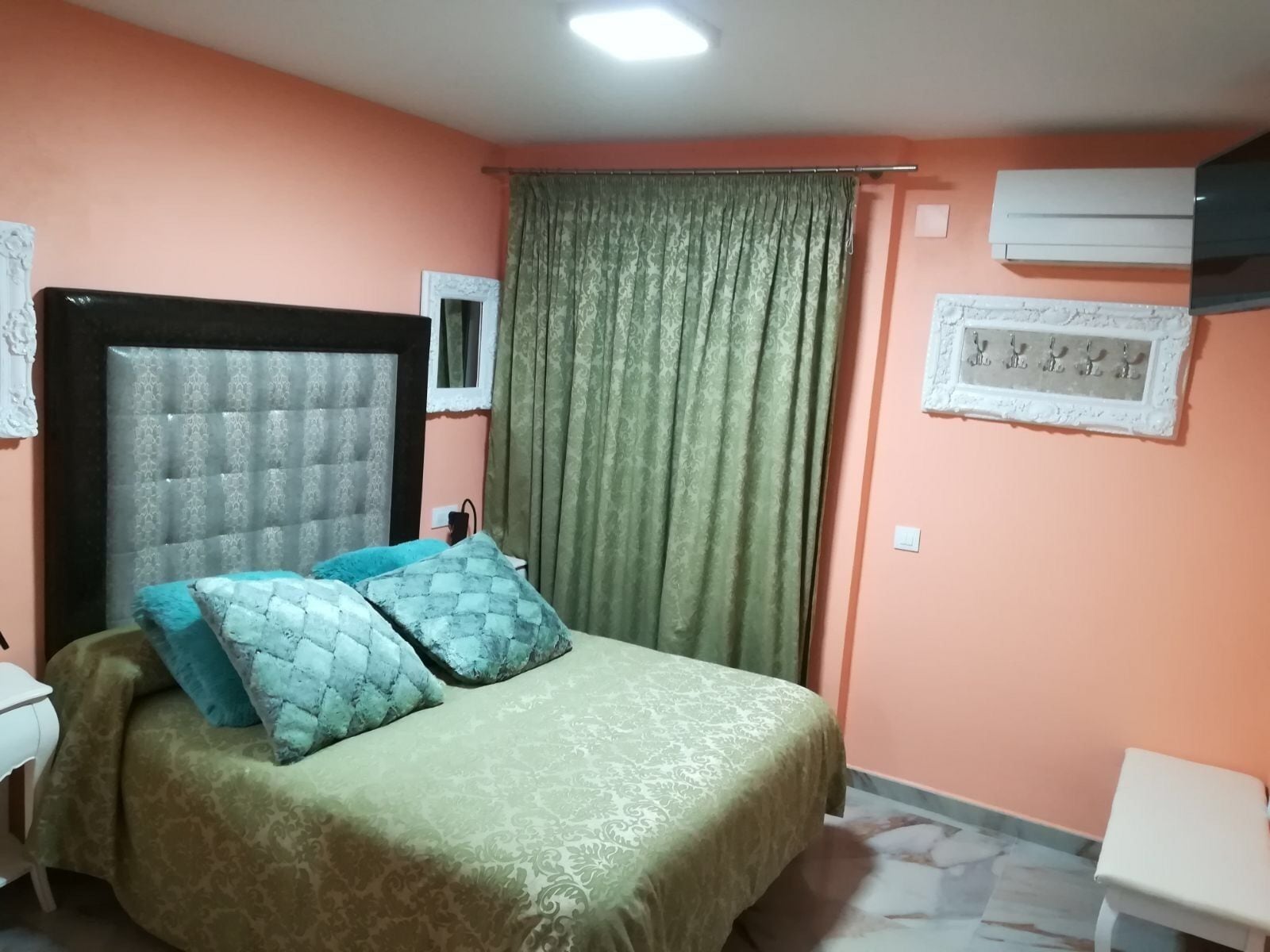 Un dormitorio con cama, mesita de noche, unidad de aire acondicionado y ventana con cortinas.