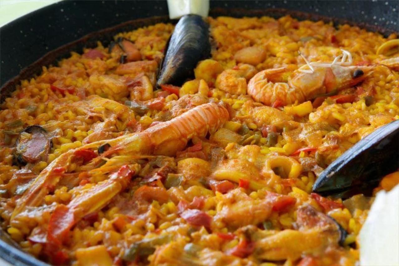 Una paellera grande y poco profunda, llena de paella de mariscos.