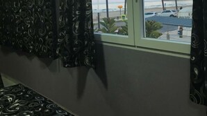 Een kamer met een groot raam met uitzicht op een strand, een bed en een gordijn met een spiraalpatroon.