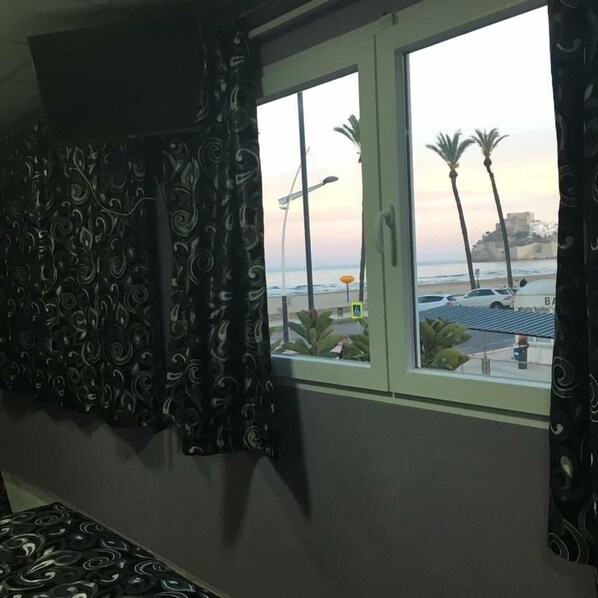 Una habitación con un gran ventanal con vistas a la playa, una cama y una cortina con un diseño de remolinos.