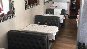 Ein Restaurant mit mehreren Tischen und Sitzecken, jeweils mit Weingläsern und Besteck gedeckt.