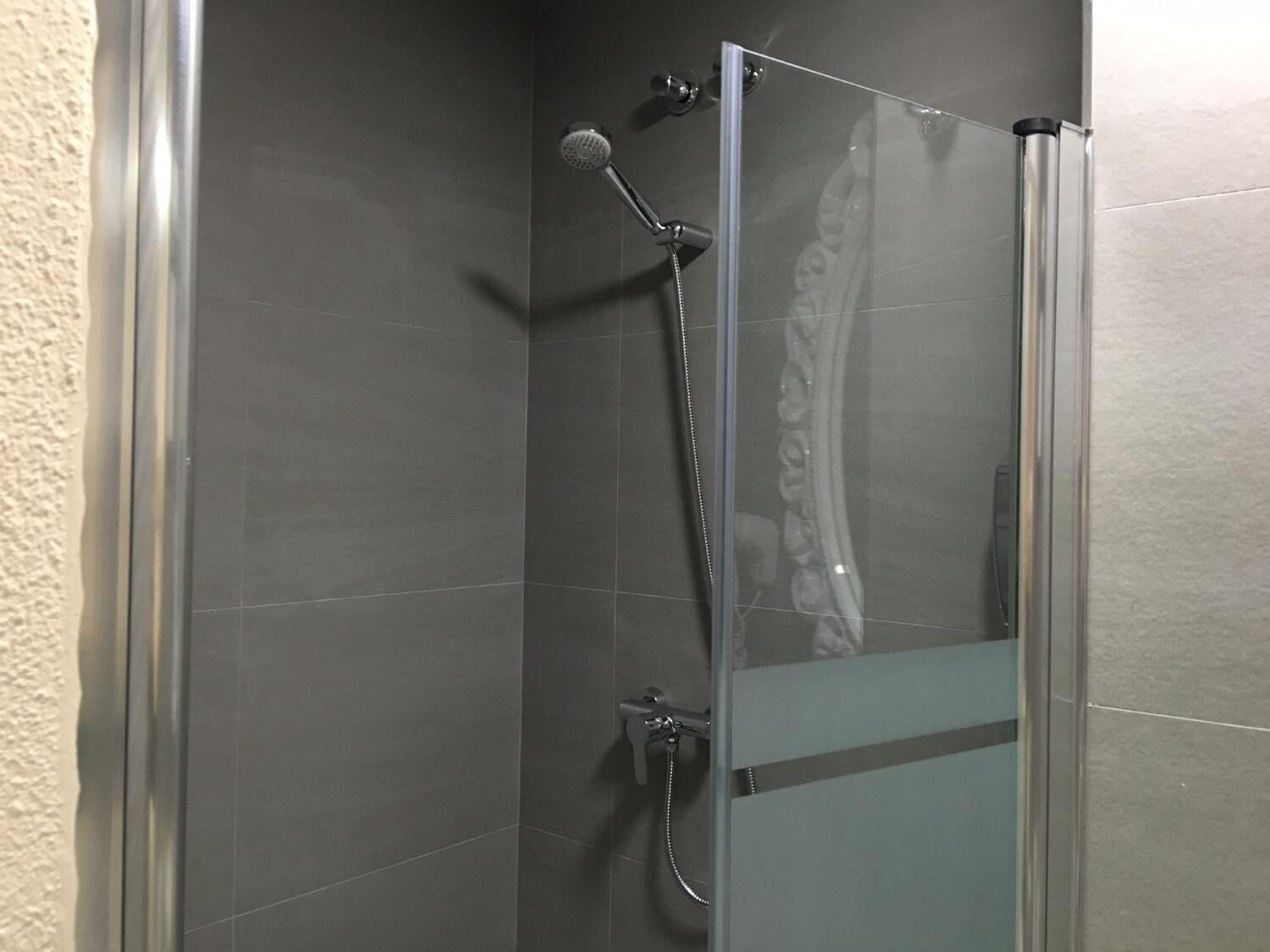 A glass-enclosed shower stall with a handheld showerhead and a wall-mounted faucet.