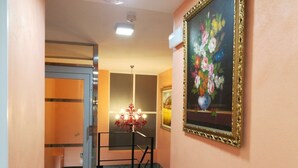 Een hal met een marmeren vloer, een kroonluchter, een bloemen schilderij en een deur naar een andere kamer.