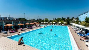 A swimming pool with people swimming and lounging, surrounded by sun umbrellas and lounge chairs. - Residence Long Beach Village (Ravenna)