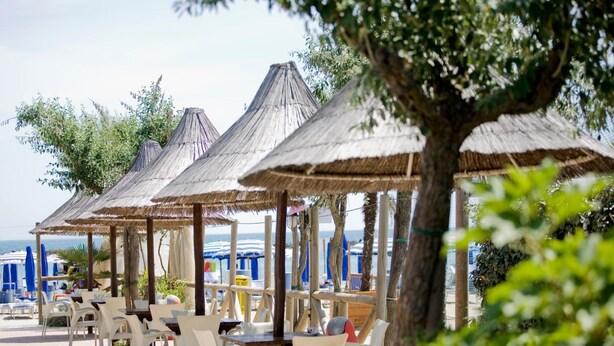 A beachside café with outdoor seating under thatched umbrellas, overlooking the sea. - Residence Long Beach Village (Ravenna)