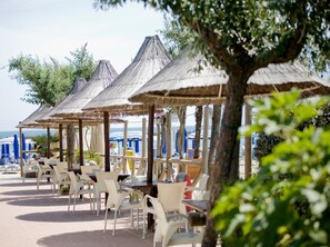 A beachside café with outdoor seating under thatched umbrellas, overlooking the sea. - Residence Long Beach Village (Ravenna)