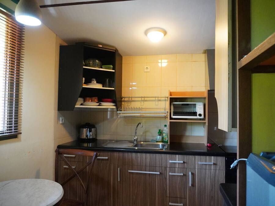 Une cuisine compacte avec des meubles en bois, un four encastré, un évier et une petite fenêtre avec des stores.