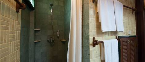 A shower area with a glass door, a towel rack with two towels, and a wooden door with a towel hanging on it.