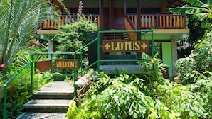 Un bâtiment sur lequel on peut lire l’inscription « LOTUS », ainsi qu’un panneau indiquant « BIENVENUE », le tout entouré d’une végétation luxuriante.