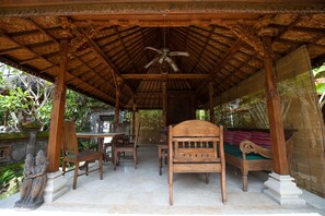 Un pavillon en bois avec un toit de chaume, un lit et un ventilateur de plafond.