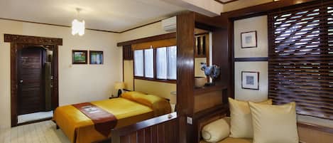 A room with a bed, a sofa, a wooden bench, and a window with blinds.