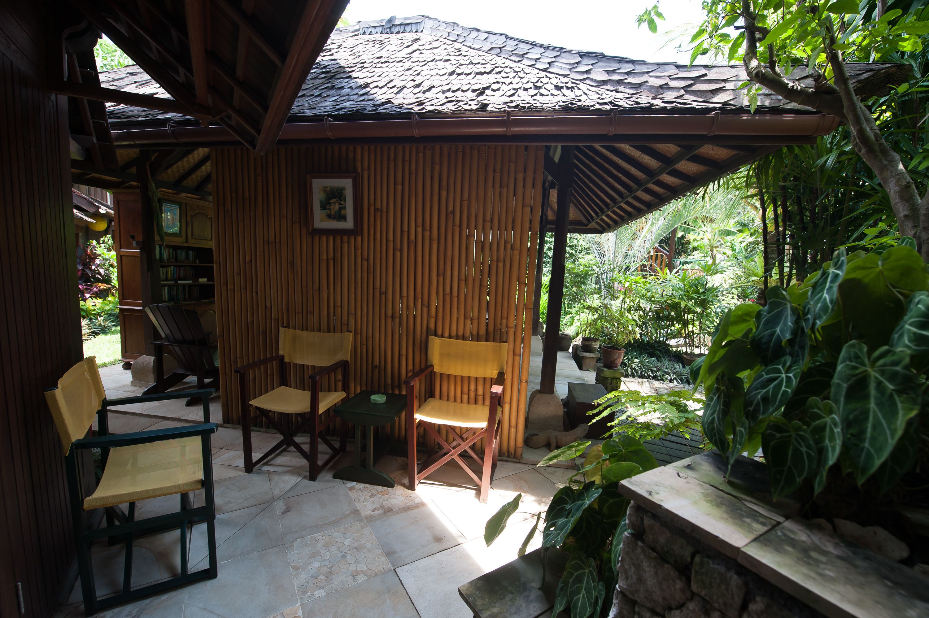 A covered outdoor seating area with bamboo walls, a tiled floor, and various chairs and tables.