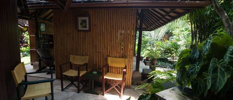 Un espacio exterior techado con paredes de bambú, piso de baldosas y diversas sillas y mesas.