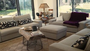 Ein Wohnzimmer mit einer Couch, einem Hocker, einem Couchtisch und Blick ins Freie.