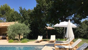 Ein Poolbereich mit Liegestühlen und Sonnenschirmen, umgeben von Bäumen und einem Gebäude mit einem Ziegeldach.