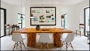 Ein moderner Essbereich mit einem großen Holztisch, weißen Stühlen und einem zentralen Kunstwerk.