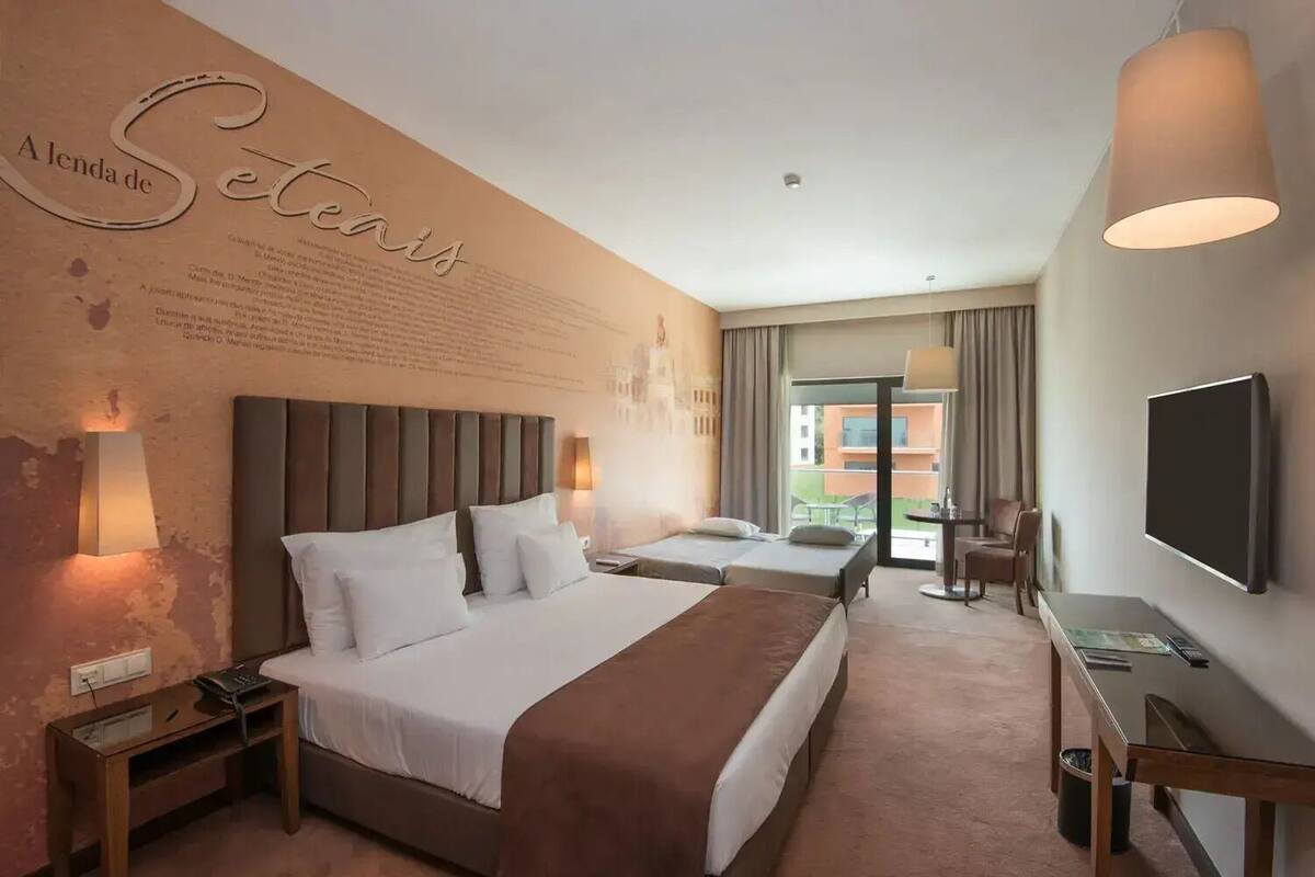 Ein Hotelzimmer mit zwei Betten, einem Fernseher, einem Schreibtisch und einem Balkon mit Blick.