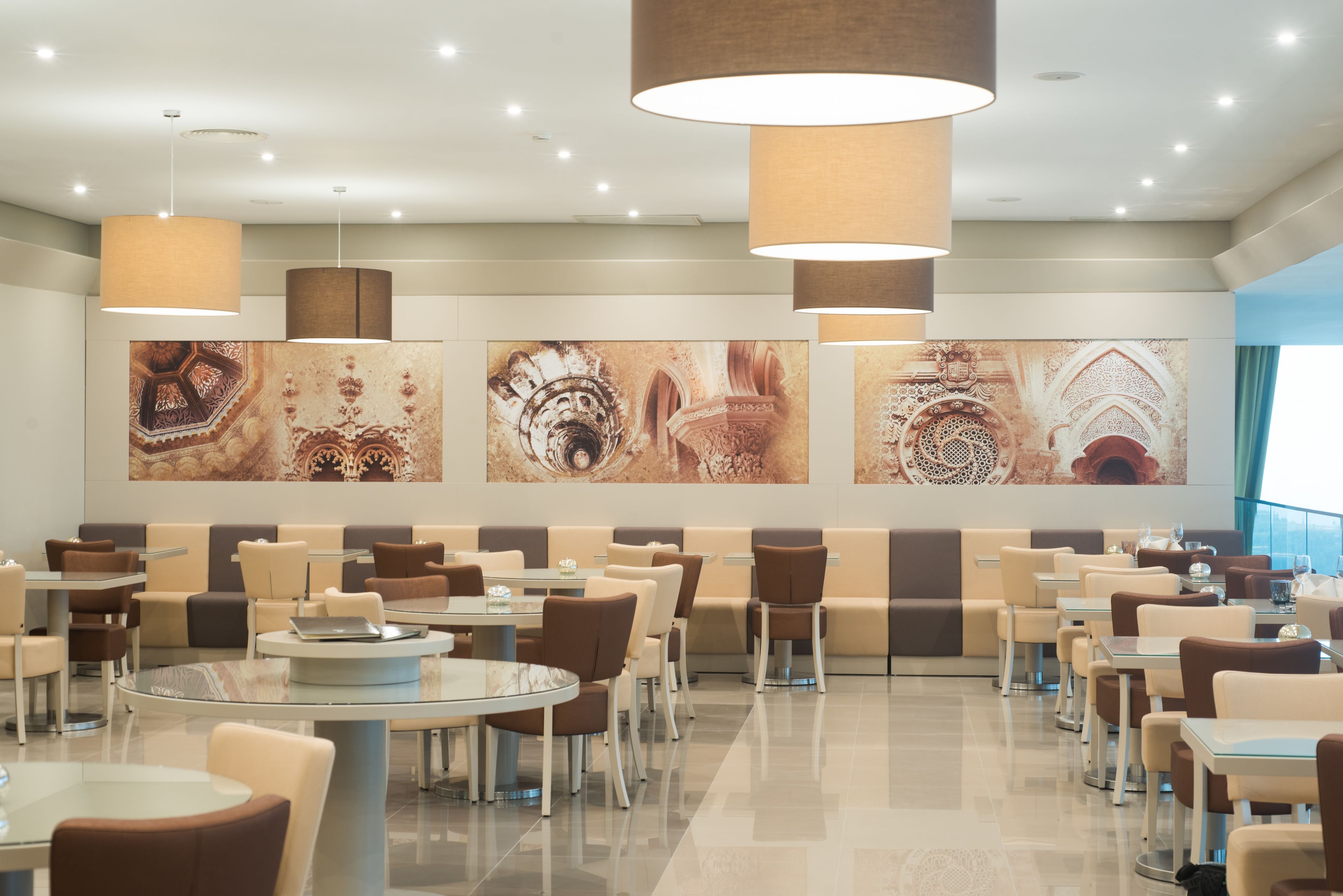 A modern restaurant with round tables and booths, featuring large wall art and pendant lighting.