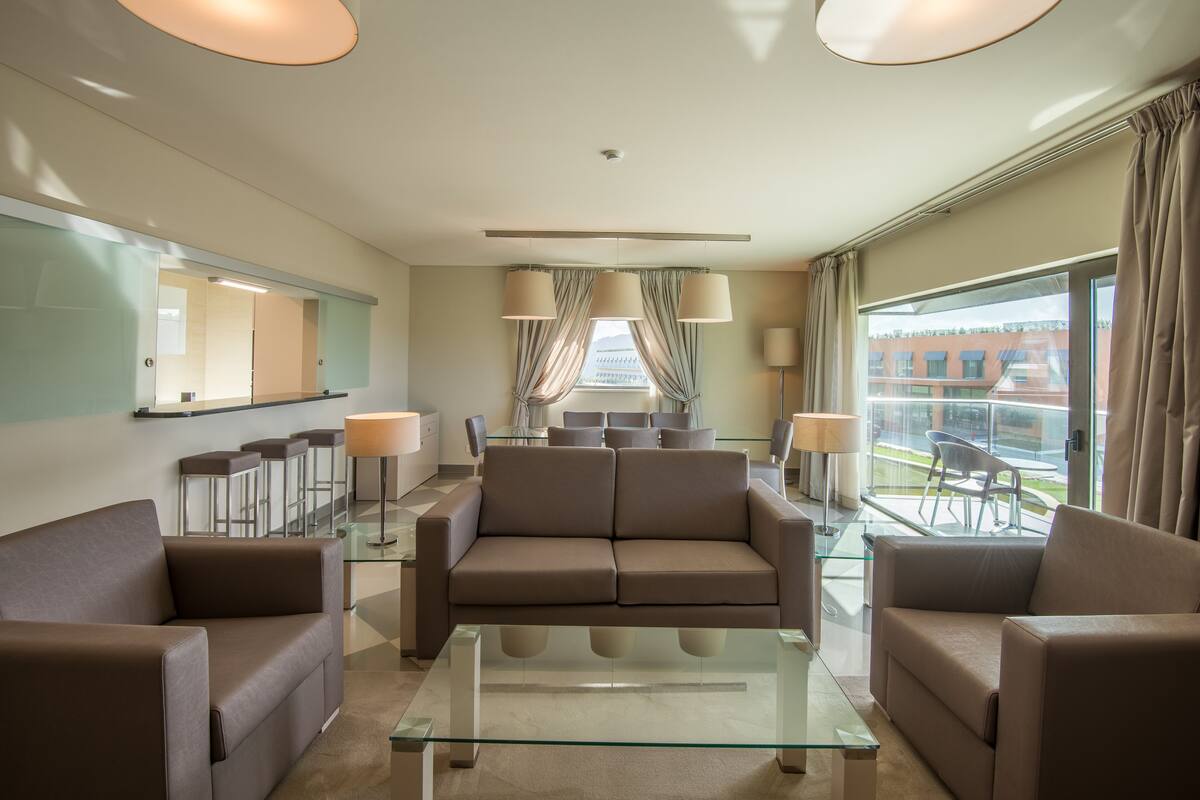 Eine moderne Hotelhalle mit einer Sofagruppe, einem Glastisch und Blick auf die Stadt durch große Fenster.