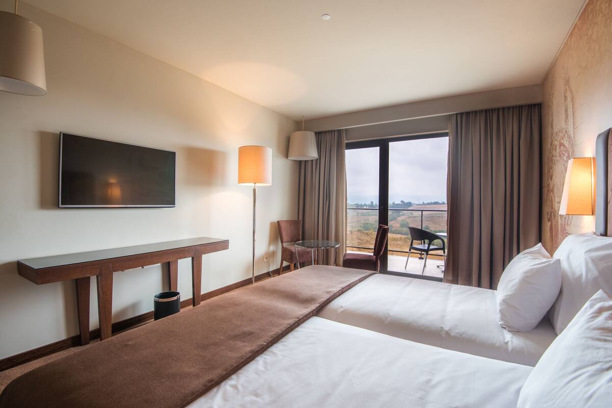 Ein Hotelzimmer mit zwei Betten, einem Fernseher, einem Schreibtisch und einem Balkon mit Blick.