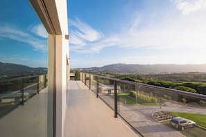 A modern balcony with a clear view of a hilly landscape and distant mountains.