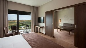 A hotel room with a large bed, a desk, a chair, a TV, and a balcony with a view of the countryside.
