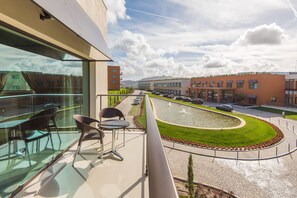A balcony with a glass railing, outdoor seating, and a view of a landscaped area with a water feature and buildings in the background. - Vila Gale Collection Sintra Hotel (Sintra)