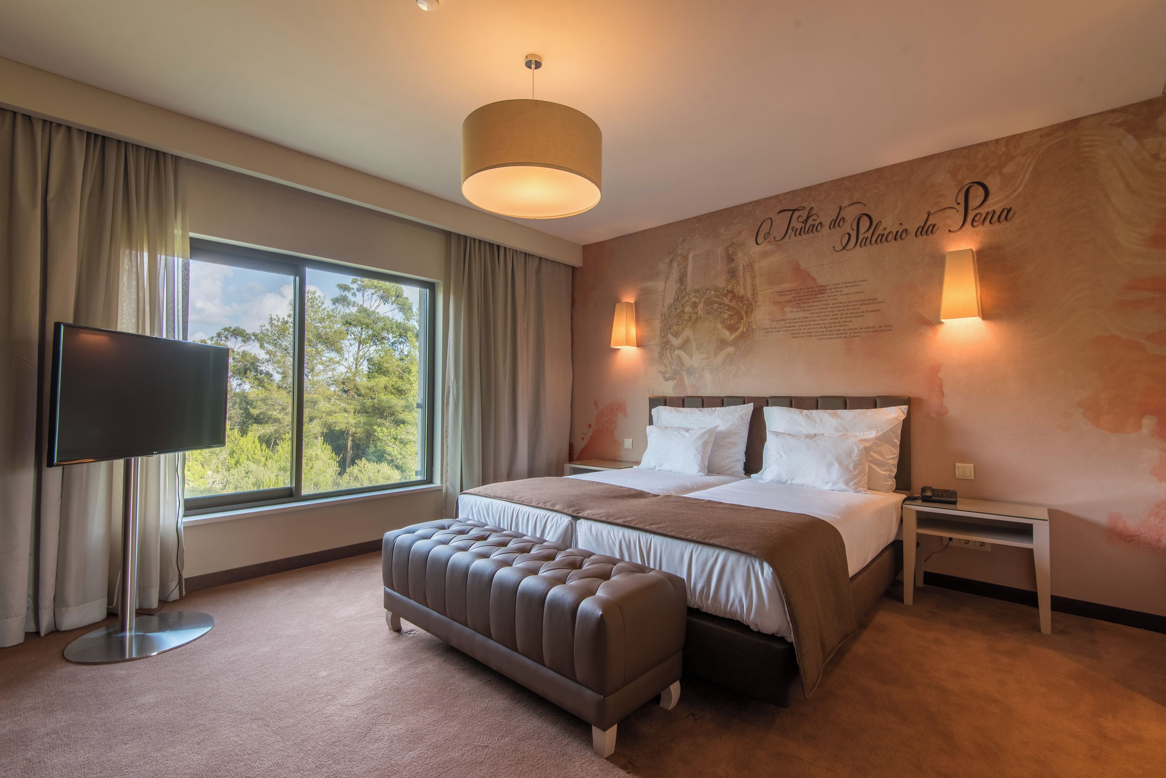 Une chambre d’hôtel dotée d’un grand lit, d’un téléviseur à écran plat, d’une fenêtre avec des rideaux, d’une lampe fixée au mur et d’un élément décoratif mural.