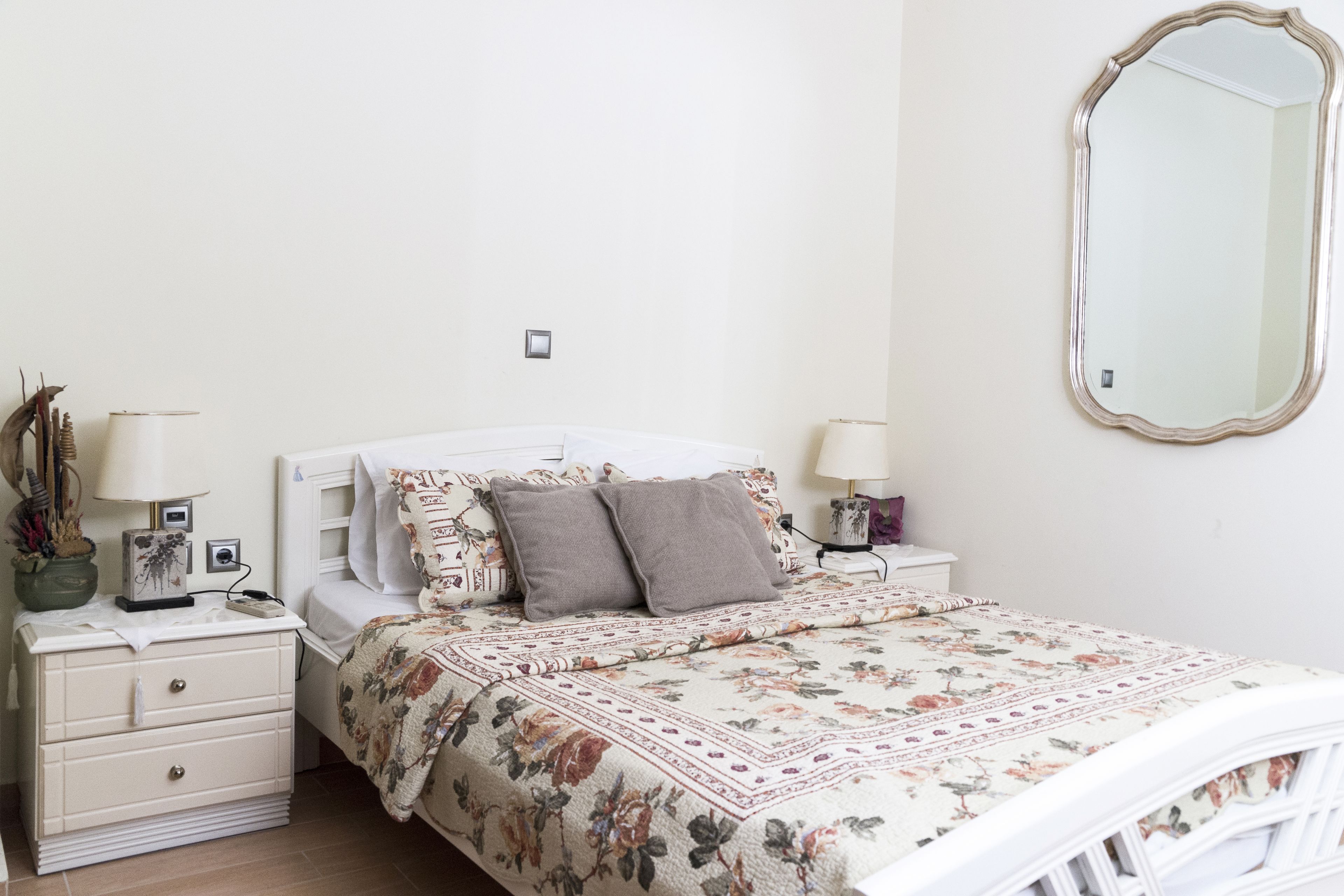 A bedroom with a floral bedspread, two bedside tables with lamps, a nightstand, and a large mirror on the wall.