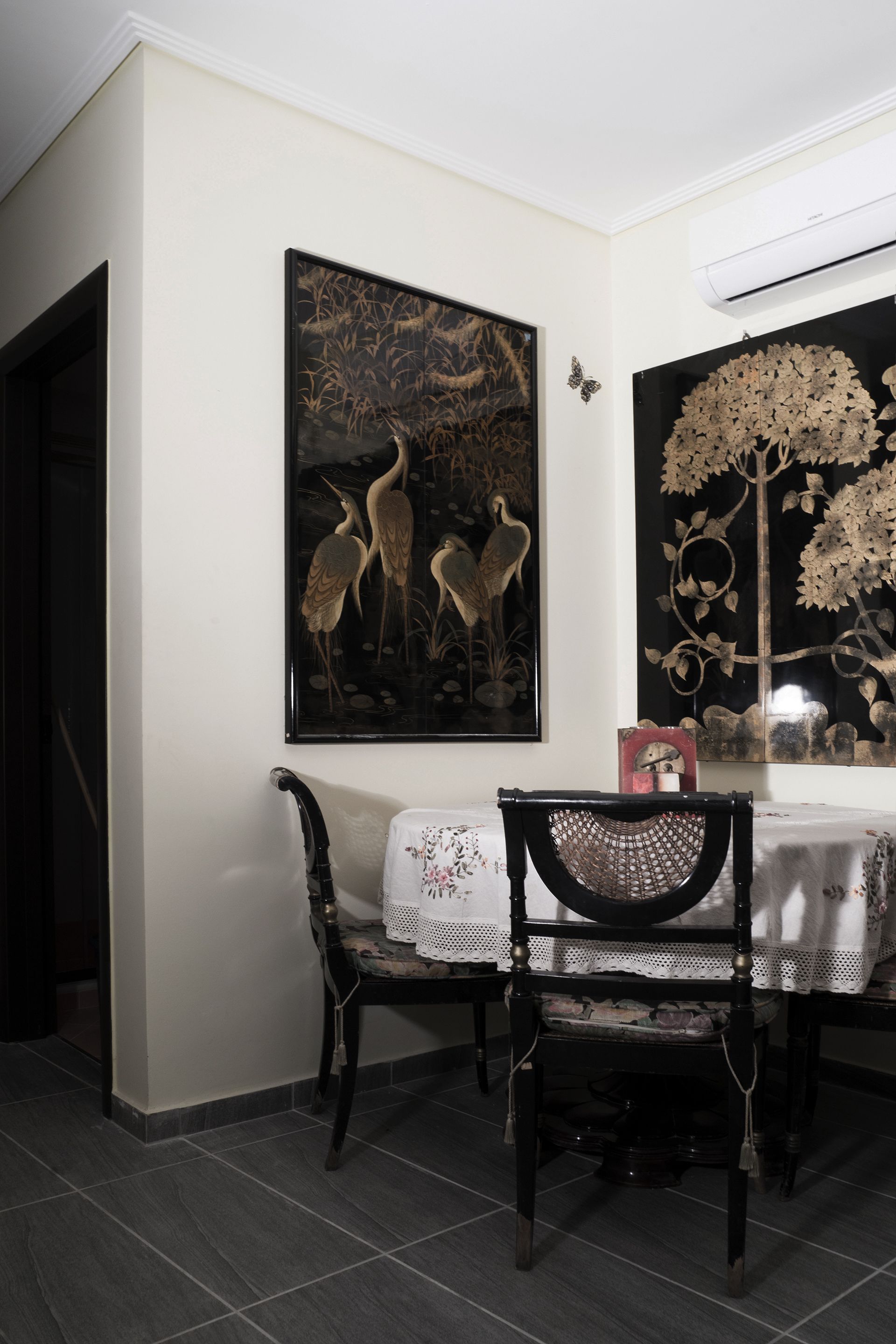 Un comedor con una mesa dispuesta para dos, una silla y una obra de arte en la pared que representa aves y un árbol.
