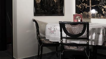 Uma área de refeições com uma mesa posta para dois, uma cadeira e uma obra de arte na parede retratando pássaros e uma árvore.